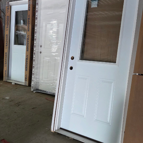 Three white doors are leaning against a wall in a warehouse. Two doors are partially wrapped in plastic packaging. The scene appears industrial and orderly.