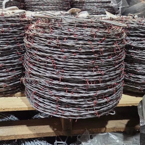 Stacked rolls of barbed wire with red-tipped barbs are neatly arranged on wooden shelves, creating an industrial and rugged atmosphere.