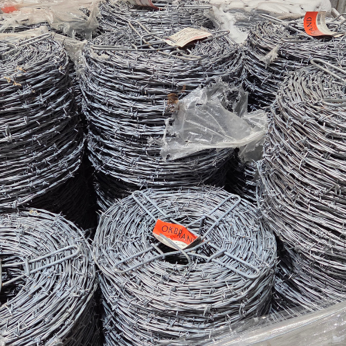 Stacks of coiled barbed wire are piled on top of each other, wrapped in plastic. The industrial feel suggests construction or fencing use.