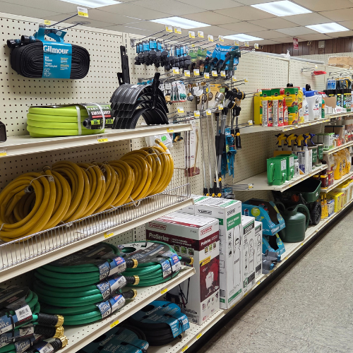Store aisle with shelves stocked with garden hoses, sprayers, and watering cans. Brightly lit, organized, conveying a practical and functional atmosphere.