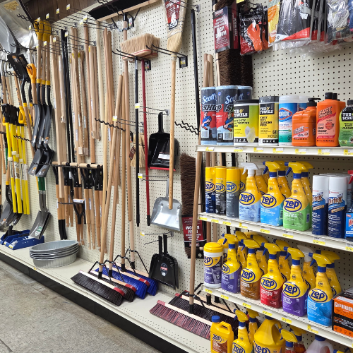 A hardware store aisle displaying an organized assortment of cleaning tools and supplies, including brooms, shovels, and cleaning products on shelves.