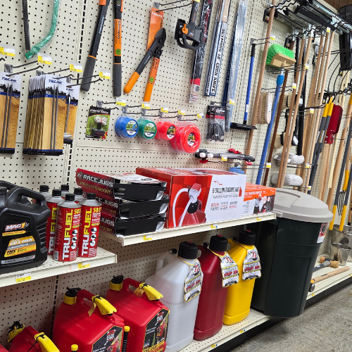 Hardware store aisle with tools and supplies. Shelves display yard tools, fuel cans, and rope. Bright, organized, with a practical, utilitarian feel.