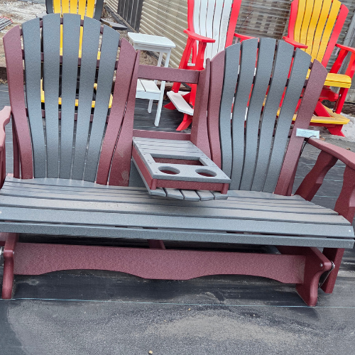 Two red and gray Adirondack chairs with a shared armrest featuring built-in cup holders, set on a wooden deck. Bright chairs are visible in the background.