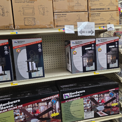 Boxes of hardware items, including ceiling fans and lights, neatly arranged on store shelves. Packaging displays images and details of the products.