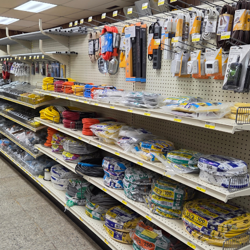 Hardware store aisle with shelves filled with colorful coiled wires, packaged cables, and electrical accessories. Bright, organized, and utilitarian atmosphere.
