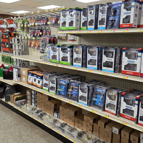 Store shelves filled with various automotive products like headlights, car parts, and tools. The setting is organized with bright lighting.