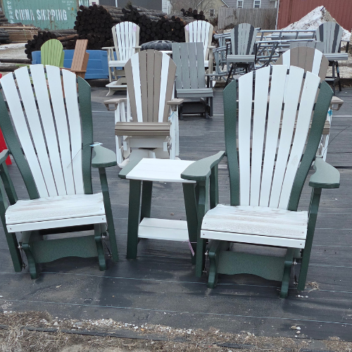 Two Adirondack chairs in white and green, with a white side table between them, displayed on a wooden deck. More similar chairs are visible in the background.