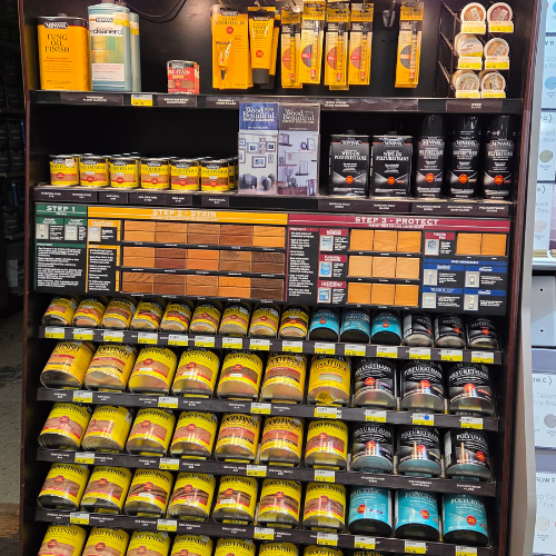 A store display of wood finishing products features a variety of stains and sealers in colorful packaging. Shelves are neatly arranged, showcasing different brands and shades for DIY projects. The overall tone conveys organization and variety.