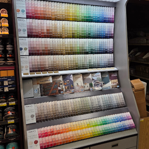 A display of paint swatches shows a wide range of colors, from vibrant to neutral shades, organized in rows. The setting appears to be a store.