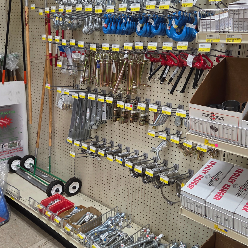 A hardware store aisle displays neatly organized tools and accessories on a pegboard. Items include wrenches, locks, and handles. Labels and prices are visible.