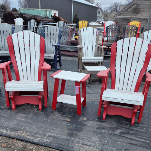 A display of colorful Adirondack chairs and tables on a wooden deck. The foreground features red and white chairs with matching tables, creating a vibrant, inviting outdoor setting.