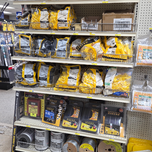 Shelves display yellow-packaged electric fencing supplies, wiring, and fencing products in a hardware store. The setting is organized and well-stocked.