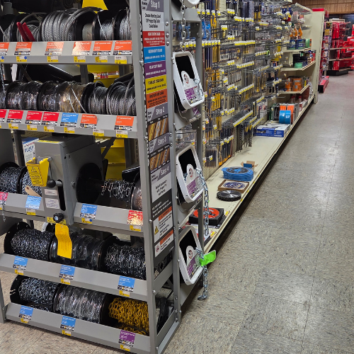 Aisle in a hardware store with neatly organized spools of wire on the left and rows of tools and accessories displayed on shelves to the right.