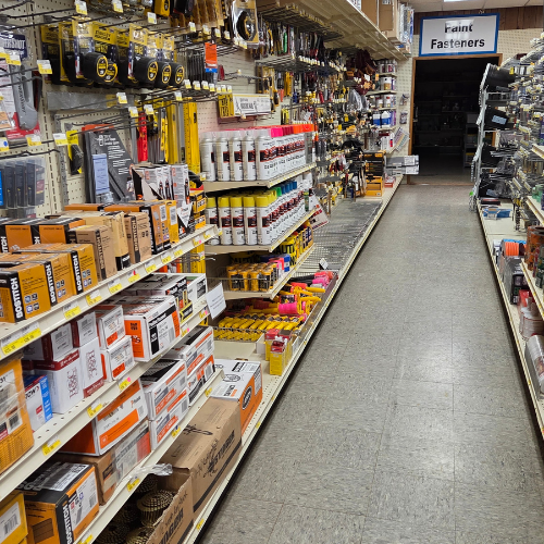 A hardware store aisle filled with painting supplies and fasteners; shelves stocked with boxes, tools, and bottles. Bright and organized ambiance.
