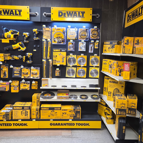 A hardware store display featuring a variety of DeWalt tools and accessories. Products include drills, saw blades, and toolboxes, all in the brand's signature yellow and black packaging, arranged neatly on shelves and pegboards. The display conveys a sense of professionalism and reliability.