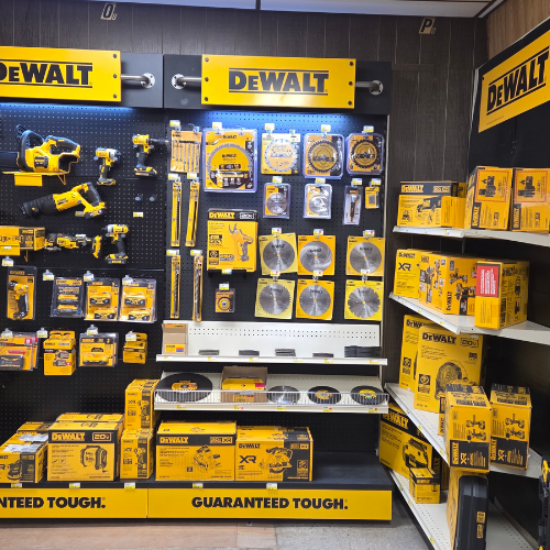 Display of DeWalt power tools and accessories on black pegboards and white shelves. Bright yellow and black packaging highlights the brand's identity.