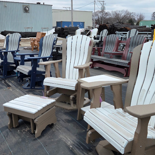 Outdoor display of Adirondack chairs in various colors, including white, gray, and blue. The scene suggests a furniture store setting on a cloudy day.