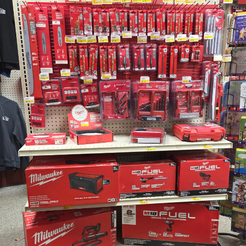 Retail display of Milwaukee power tools and accessories in bright red packaging. Hanging tools and stacked boxes create an organized and vibrant presentation.
