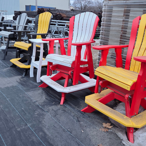 A row of colorful Adirondack chairs on a paved surface. Bright red and yellow hues stand out against the muted, overcast background, creating a lively atmosphere.