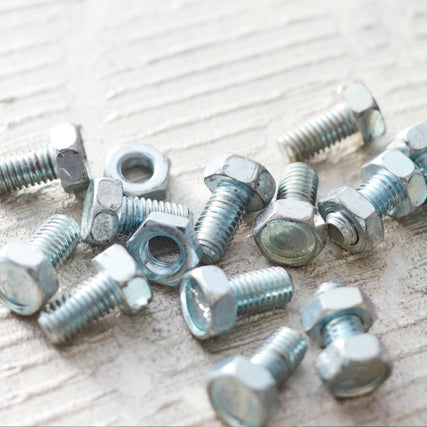 HardwareA scattered group of shiny metal bolts and nuts on a textured surface, reflecting light. The image conveys an industrial and organized tone.